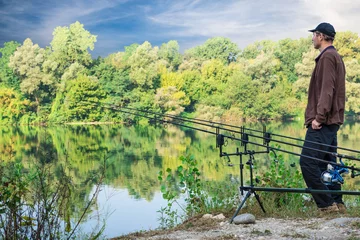 Fototapeten Fishing adventures. Fisherman and carp fishing gear in a sunny day © AleMasche72