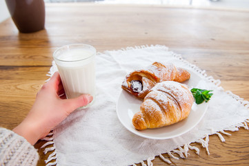 Close up young girl having breakfast - fresh croissant, bun with fruits and glass of milk. Selective focus. Morning concept