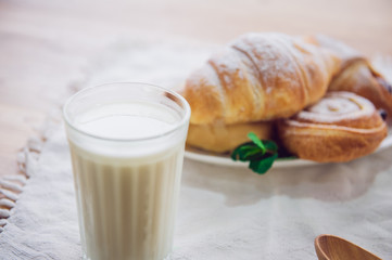 Glass of milk and plate with assortment of various fresh pastries on the background. Breakfast concept, selective focus