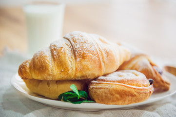 Close up continental breakfast with assortment of fresh pastries and glass of milk on the background. Selective focus