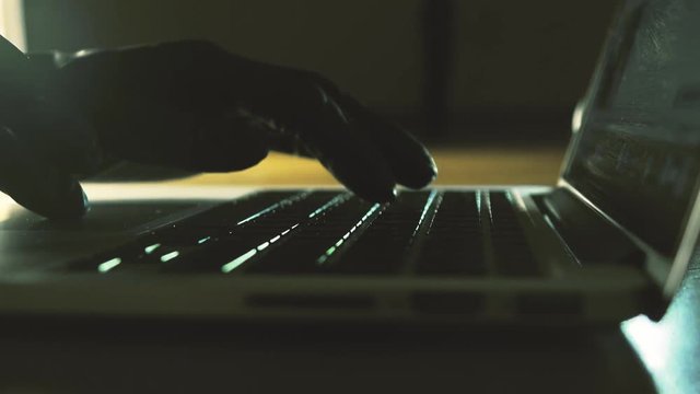 Person wearing black gloves typing on laptop keyboard. Hacking, stealing, secrecy, espionage concepts. 4K close-up shot