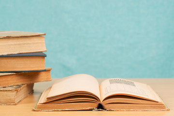 Open book, stack of hardback books on wooden table.
