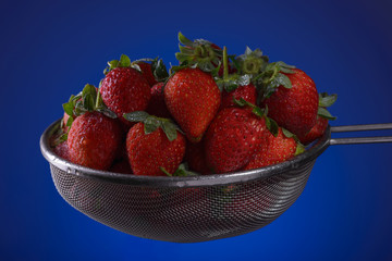 Fresh strawberries in a colander on a blue background