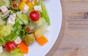 Greek salad in white glass dish plate, closeup from the top. Olives, tomatoes, paprika, bell pepper, cucumber, onion, feta cheese, olive oil. Standing at wooden background macro.