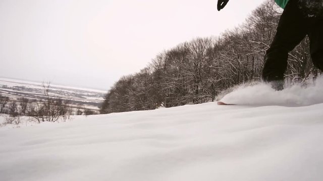 Young man snowboarder in green suit slides down snow forest slope