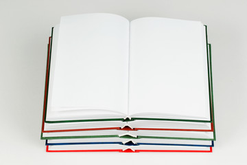 Open book, stack of hardback books on table.