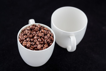 Coffee beans in coffee mug on black background, one full, one empty