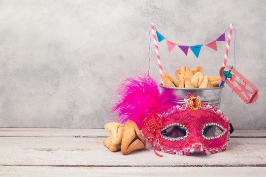 Purim holiday concept with hamantaschen cookies or hamans ears in bucket and carnival mask over rustic background