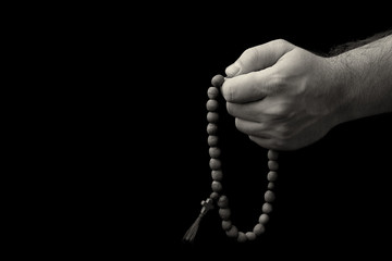 Rosary in male hands on a black background