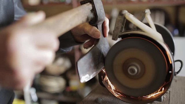 Old man sharpening his ax on a grinder in an workshop
