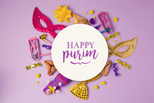 Purim holiday concept with white paper circle and party supplies on purple background. Top view from above