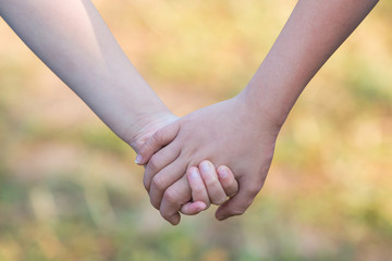 Kids' hands holding for support and friendship, blur green grass