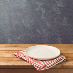 Empty white plate on wooden table over blackboard background