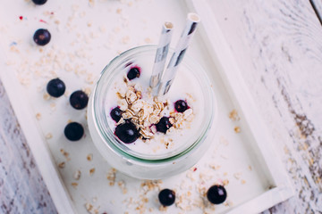 Delicious Healthy breakfast or snack. Yogurt with berry black currant, oat flakes and mint in glass on white wooden table background. Top view, copy space