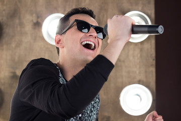 Male singer in sunglasses sings on scene in projectors lights