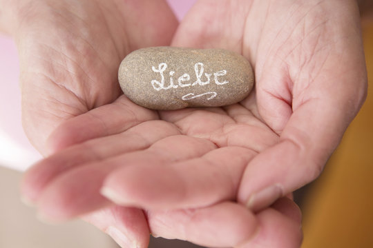 womans hands holding a stone with german word for Love