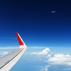 Oncoming flight traffic in mid air. Aircraft flying above beautiful earth, clouds. Aerial view of clear blue sky, aircraft wing from cabin through plane window. Travel tour background with copy space