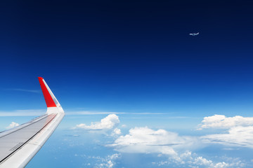 Naklejka na ściany i meble Oncoming flight traffic in mid air. Aircraft flying above beautiful earth, clouds. Aerial view of clear blue sky, aircraft wing from cabin through plane window. Travel tour background with copy space