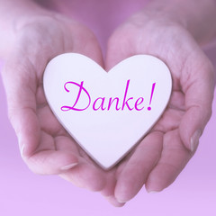 womans hands holding white heart with german word for Thank You