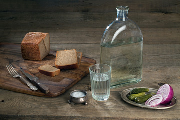 glass with vodka,cucumbers, onion and bread on a wooden table