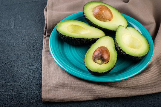 Sliced avocado in a blue plate on dark background. Vegetarian  food concept.