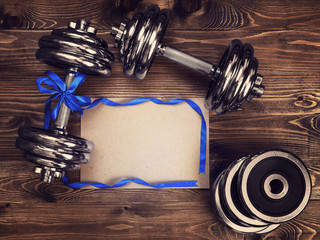 Toned image of metal dumbbells, blue atlas ribbon and a sheet of craft paper on a wooden background - 136733638
