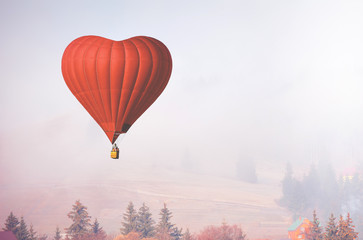 Red air balloon in shape of heart fly above forest in foggy morning. Romantic postcard background...