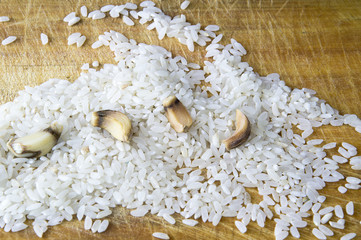 Raw rice and four cloves of garlic in the background of a kitchen board