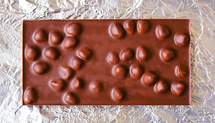 Chocolate bar with hazelnuts on a foil, closeup