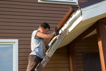 man attaches gutter on roof of porch