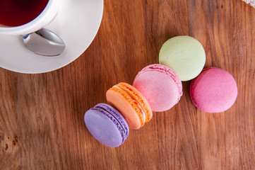 Close up of france dessert colourfull macaroons and cup of tea on wooden table in cafe. Selective focus