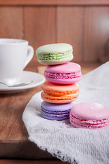 Close up of france dessert colourfull macaroons and cup of tea on wooden table in cafe. Selective focus
