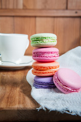 Close up of france dessert colourfull macaroons and cup of tea on wooden table in cafe. Selective focus