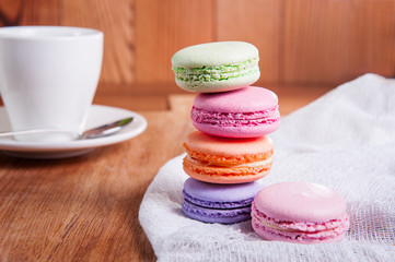 Close up of france dessert colourfull macaroons and cup of tea on wooden table in cafe. Selective focus
