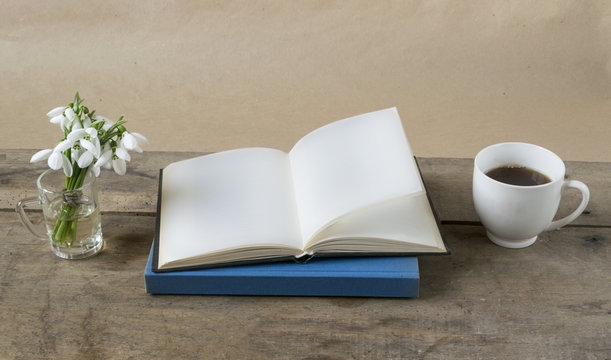 Book with empty pages, snowdrops and cup of coffee on wooden table.