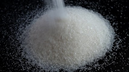Sweet sugar or salt pour back of heap on black background. Bunch of spilled white sand sugar
