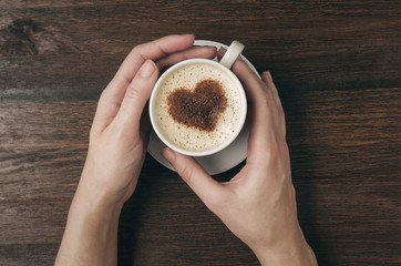 Female hand hold coffee cup with heart shape on wooden table