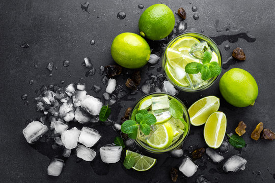 Summer mint lime refreshing cocktail mojito with rum and ice in glass on black background top view