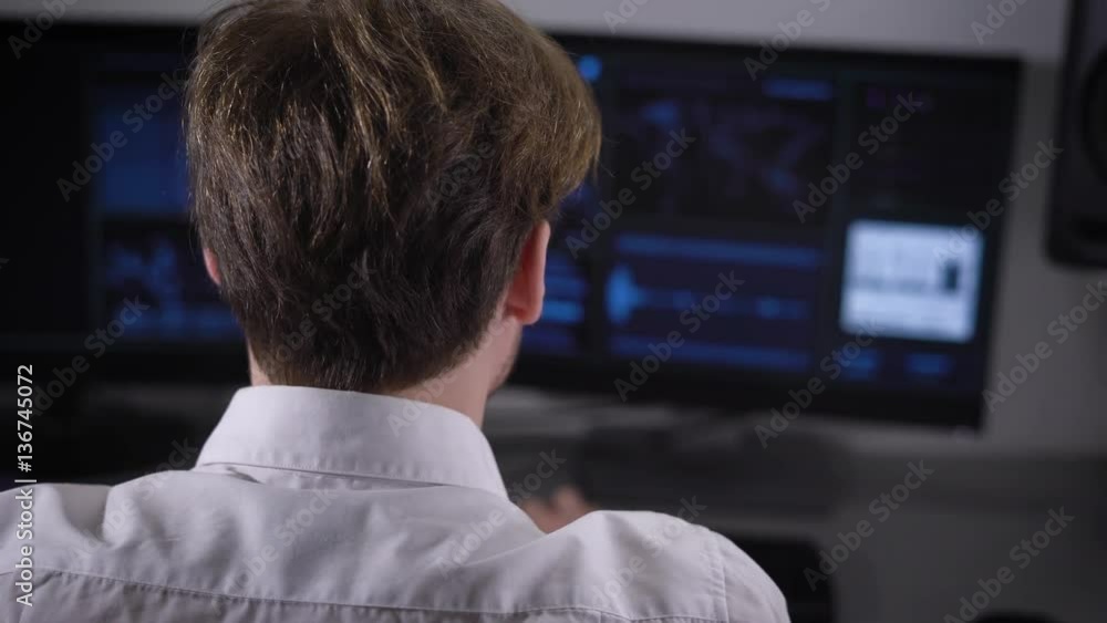 Poster experienced it specialist works on a new program on two computers. young man in glasses and white sh