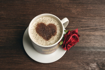 Coffee cup with heart shape and red rose on dark background
