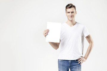 Hipster man model standing with blank sheet in hands, isolated on white background, wearing jeans and t-shirt. Space for design layout.