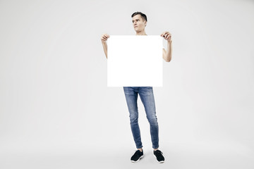 Handsome guy full-length standing with blank big poster or sheet in hands, isolated on white background, wearing jeans and t-shirt