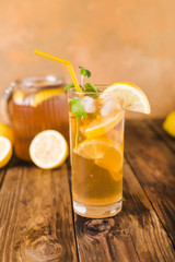 Lemon ice tea on brown wooden table with lemons around. Iced tea with lemon slices and mint on rustic background