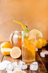 Lemon ice tea on brown wooden table with lemons around. Iced tea with lemon slices and mint on rustic background