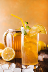 Lemon ice tea on brown wooden table with lemons around. Iced tea with lemon slices and mint on rustic background