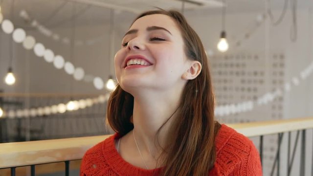 A cute young woman smiles at the camera on coffe-shop background close up