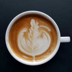 Top view of a mug of latte art coffee on black background.