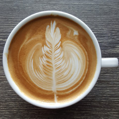 Top view of a mug of latte art coffee on timber background.