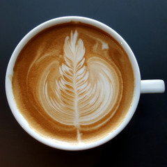 Top view of a mug of latte art coffee on black background.