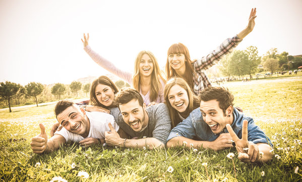 Friends group having fun together with self portrait on grass meadow - Friendship youth concept with young happy people at picnic camping outdoor - Warm vintage filter with backlight contrast sunshine